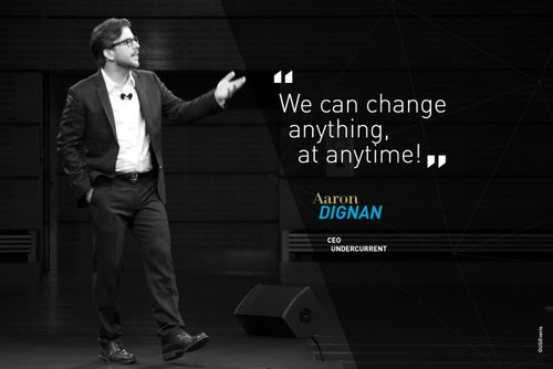 Photo d'Aaron Dignan sur scène à la conférence USI 2015 avec citation "We can change anything ar anytime"
